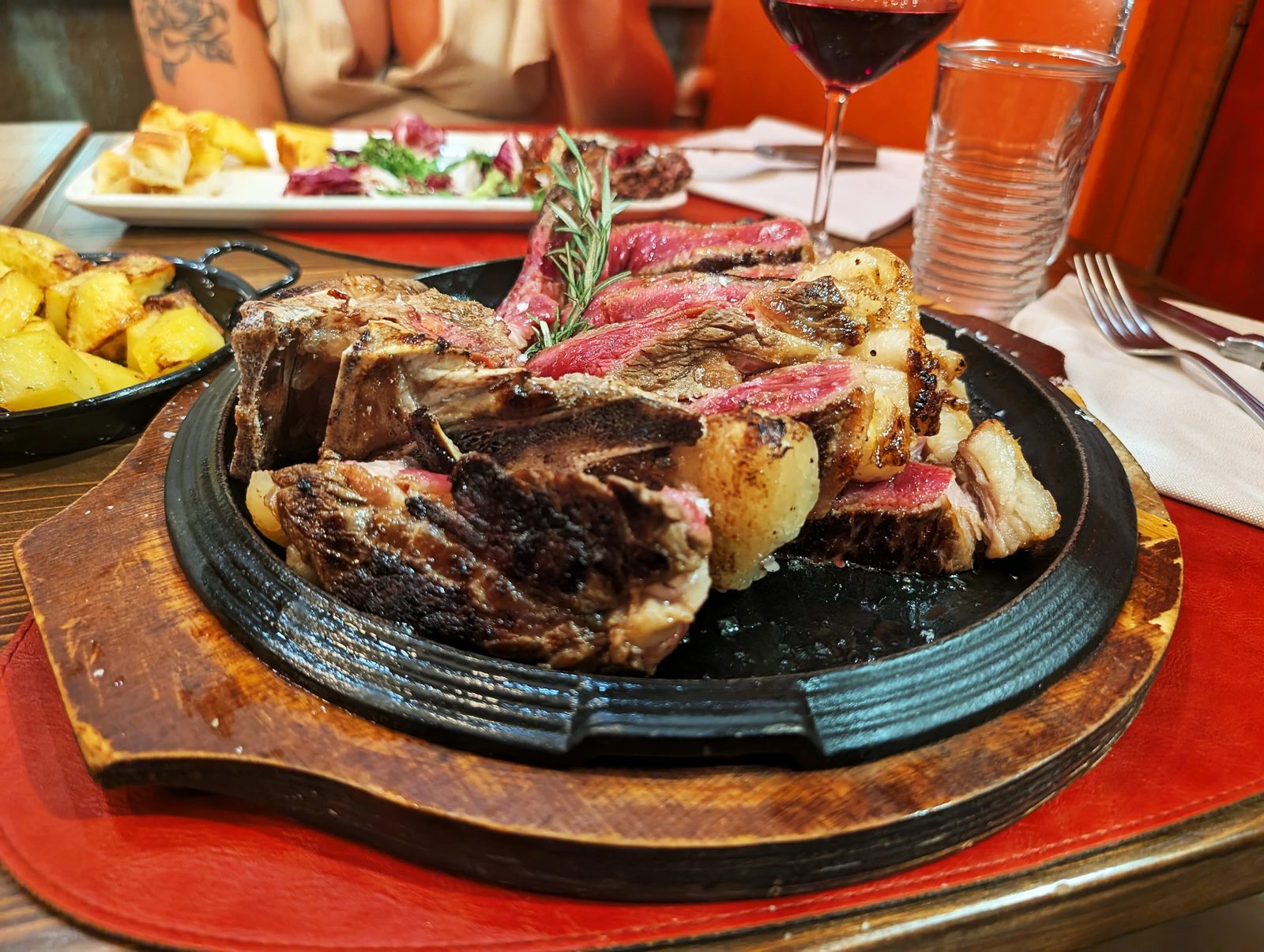 1.2 kg Fiorentina sliced on cast iron with roast potatoes and a glass of wine — Fiorentina Menu for 2